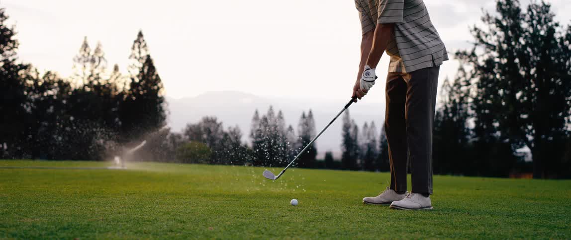 A man holding a golf stick trying to hit the golf ball with water sprinkling in the background