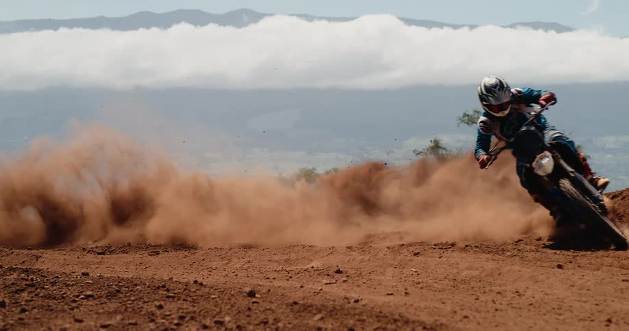 The video which appears to be stock footage based on the filmsupply watermark shows a person riding a dirt bike aggressively around a sharp turn on a reddishbrown dirt track the bike slides kicking up a dramatic large cloud of red dust that obscur