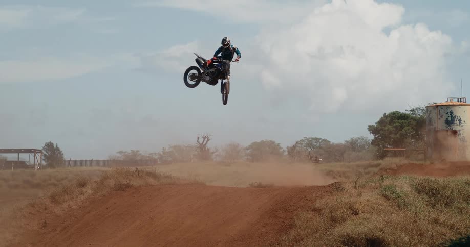 Motorcyclist jumps over dirt track under partly cloudy sky