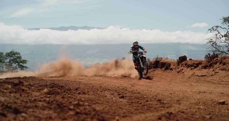 A sports athlete rides a dirt bike along a motocross track at midday speeding across the dirt path