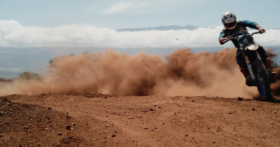 Motocross rider kicks up dust while turning on dirt track with mountains in the background