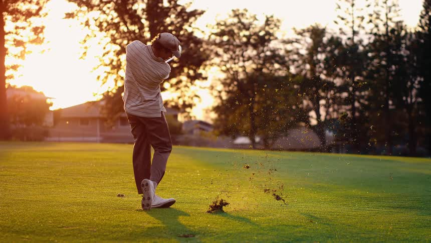 A young man swings at a golf ball on a sunny day while playing on a golf course