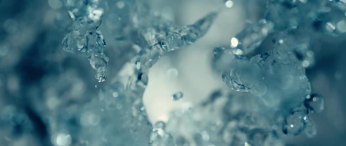 This is a slowmotion closeup shot of water splashing and raining down showing many individual droplets and streams glistening against a muted bluegray background the focus is on the dynamic chaotic movement of the clear coldlooking water