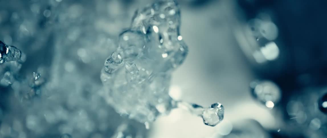 A slowmotion macro shot captures crystalclear water droplets and streams cascading against a bright hazy bluetoned backgroundthe individual water forms appear distorted and sculptural as they rise and fall emphasizing the fluid and dynamic movem