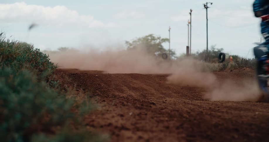 Motocross rider performs wheelie on dirt track with front wheel lifted