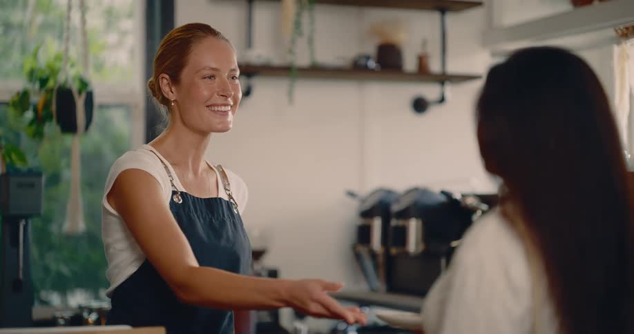 Smiling barista hands dessert plate to customer in modern caf with natural light and cozy atmosphere