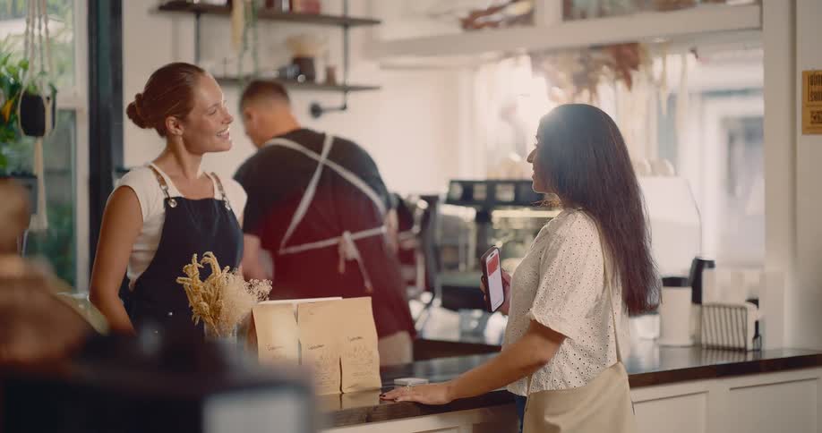 Woman with phone chats with smiling barista in bright caf with modern decor