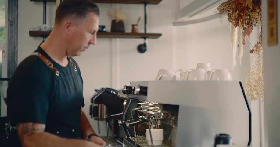 The man working in the coffee shop is using the coffee machine
