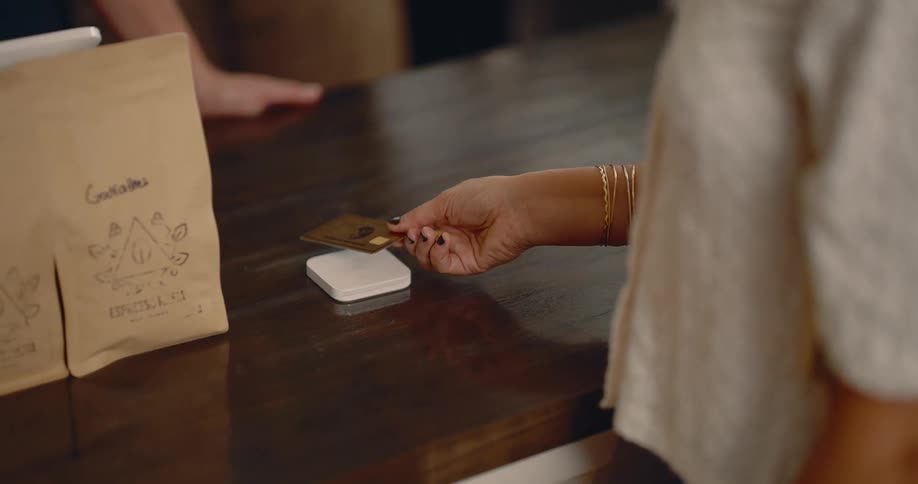 Hand of a lady placing a card on a white payment terminal on a wooden table