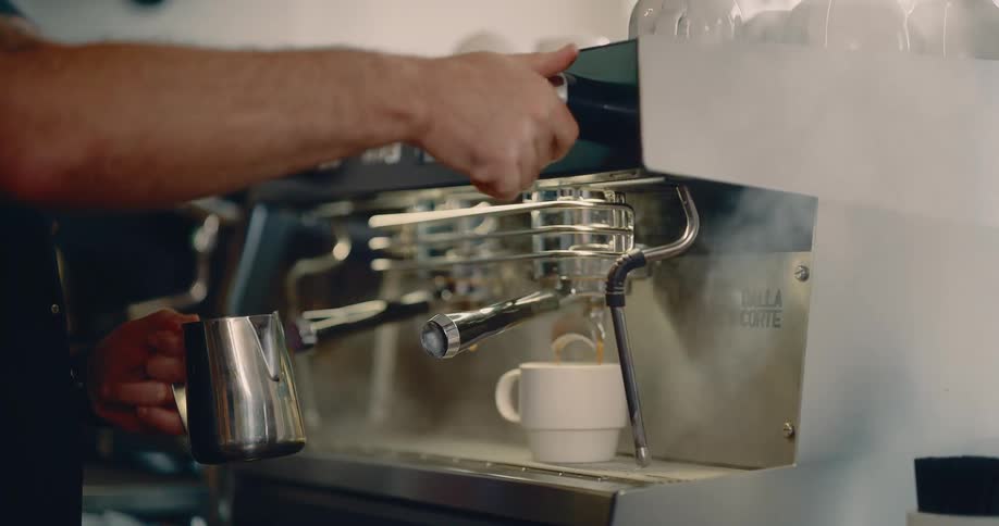 Dalla corte espresso machine brews coffee as barista holds metal pitcher beside control panel