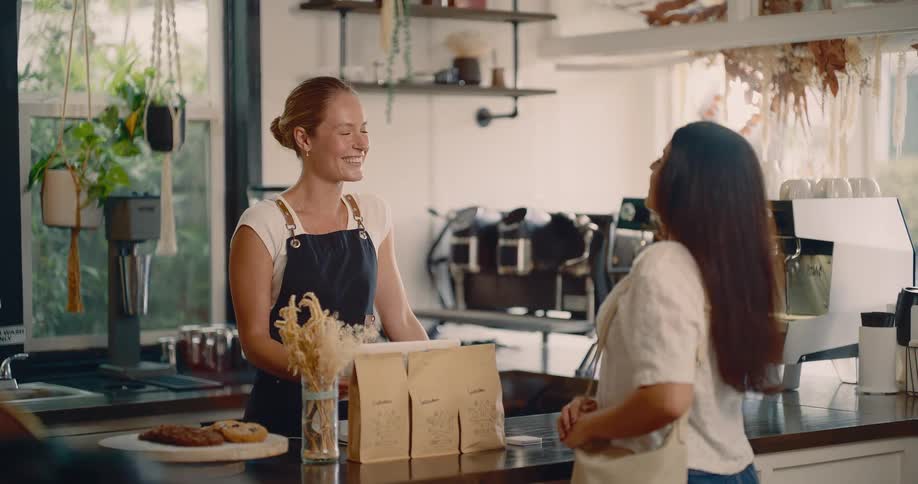 A young woman enters a caf at midday smiling at the cashier who smiles back as she asks about the product she wants