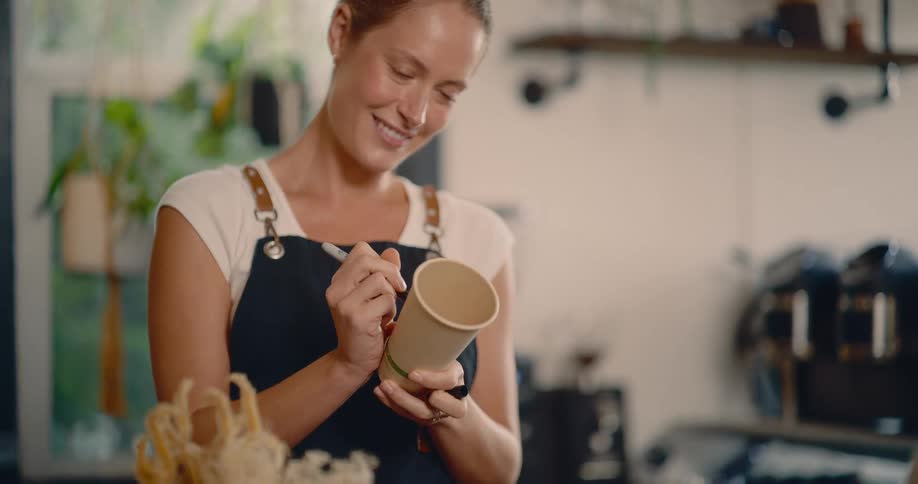A smiling woman writes on a coffee cup and placed it on a cabinet