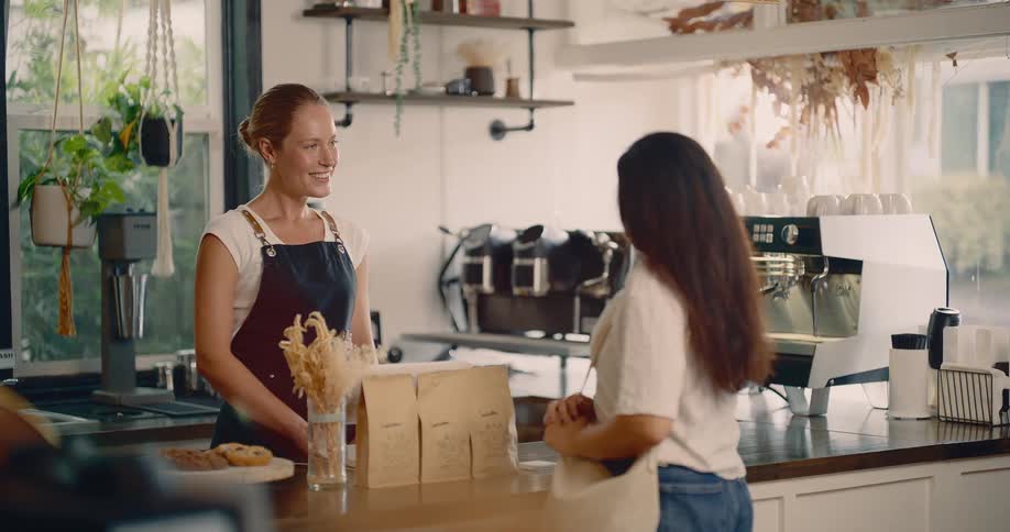 A smiling barista greets a customer at a coffee shop counter