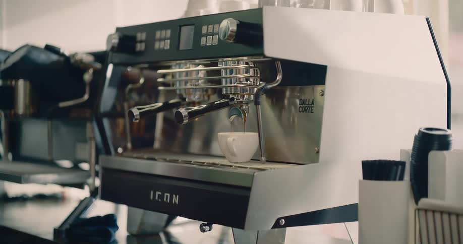 A barista wipes down the stainless steel espresso machine in a cafe while coffee brews