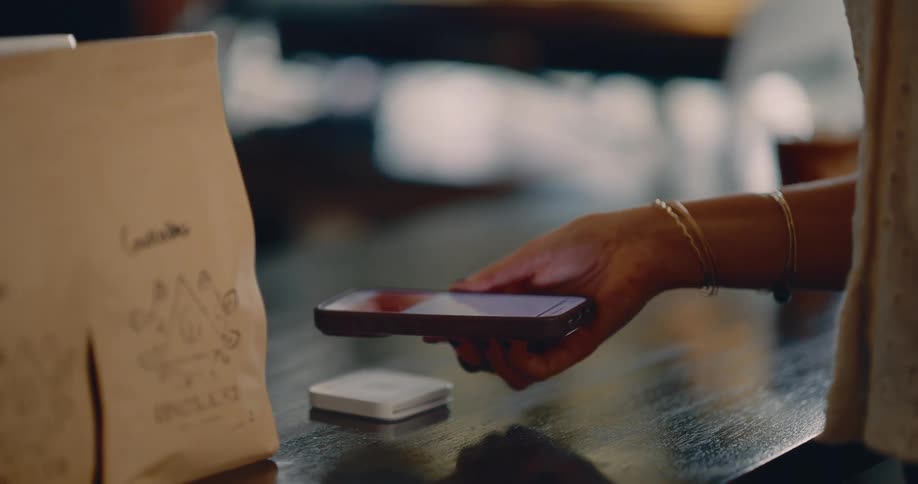A woman slides her phone across a device inside a store at midday making a payment