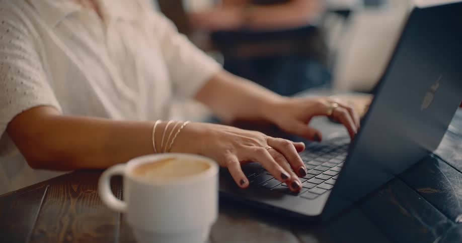 Woman typing on a laptop computer with a cup of coffee on the table