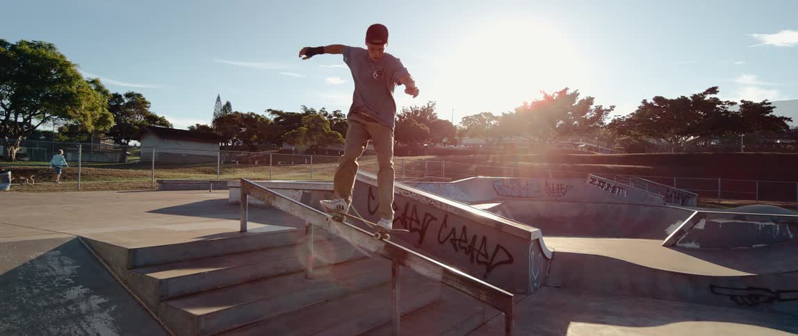 A teenager rides his skateboard on a rail at a skate park