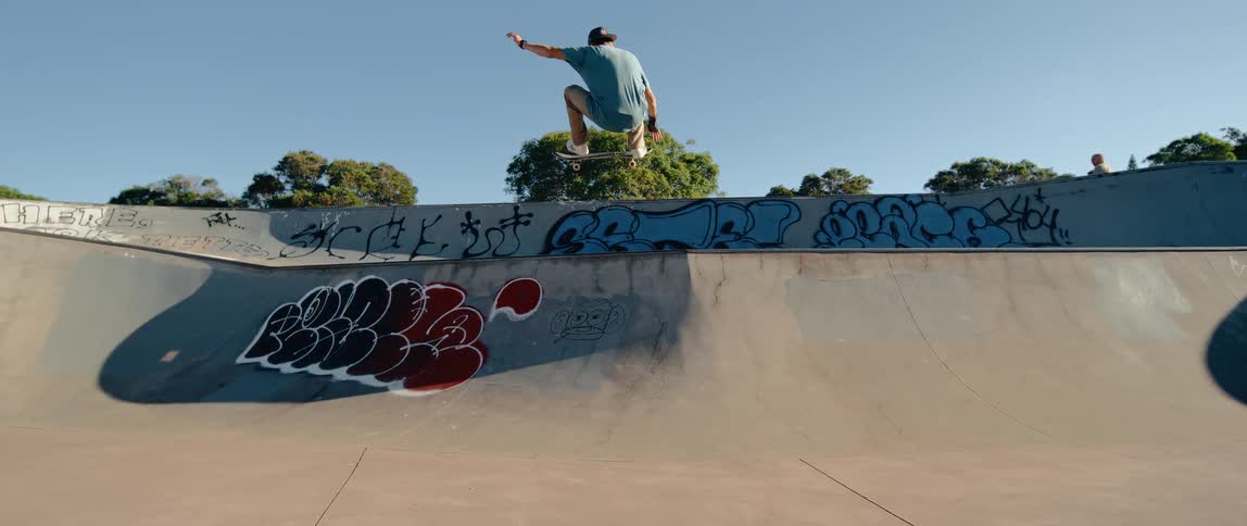 A skateboarder soars mid air off a ramp arms outstretched under a clear blue sky