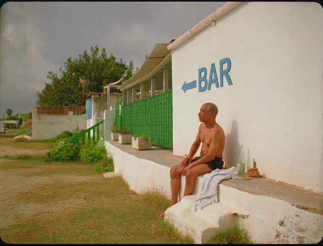 The man is sitting outside the bar with a bottle