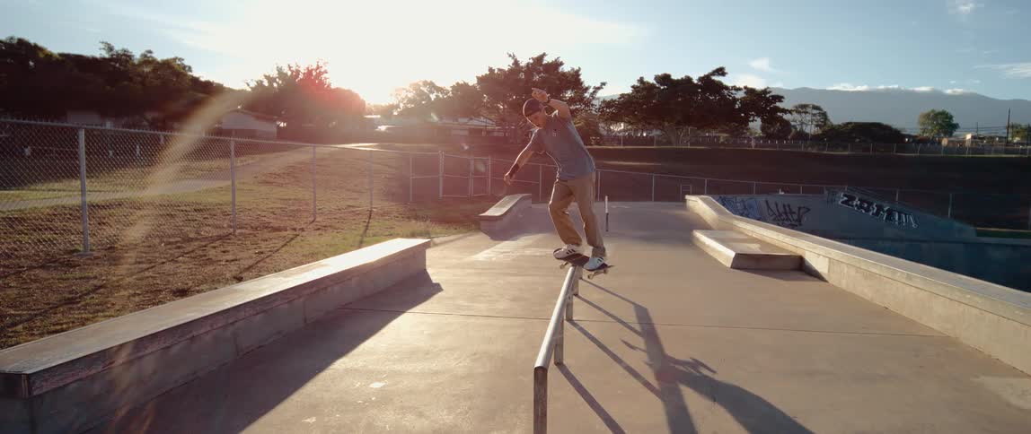 Skateboarder slides on metal rail at sunset in park surrounded by graffiti and mountains