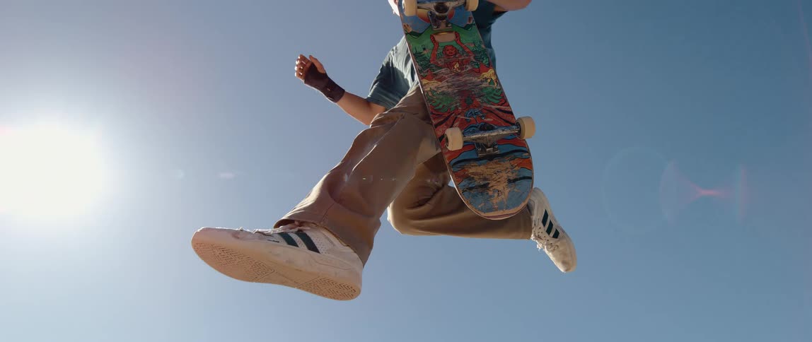 Skater jumps with graphic deck beneath sunlit blue sky