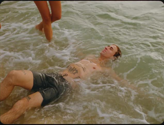 Person lying in shallow water receives gentle waves as another stands in the background