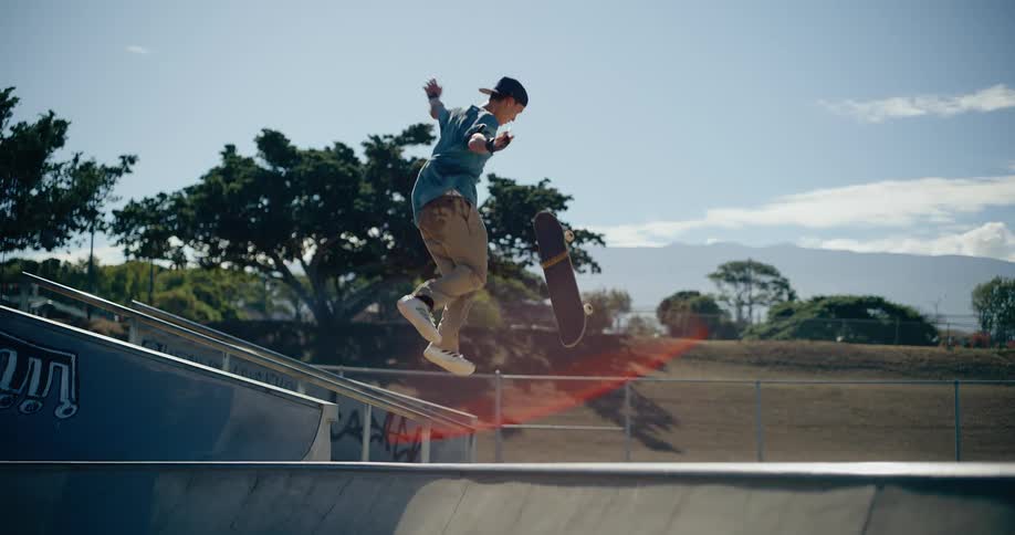 Skateboarder performs aerial trick above ramp on sunny day with blue sky and mountains behind
