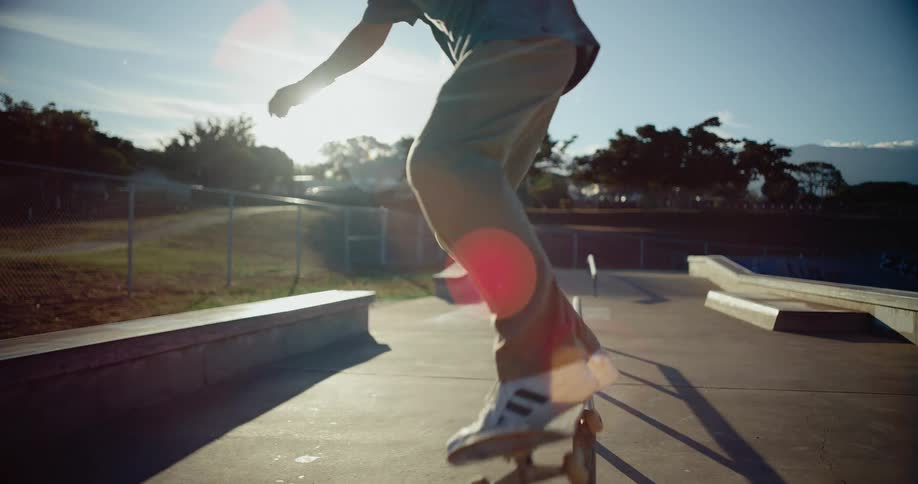 A skateboarder is captured performing a grind trick sliding across a metal rail in a sunny skate park the camera follows the action resulting in a blurred background and a lens flare from the bright sunlight