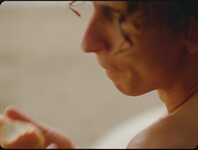 A man with wet curly hair eats a pear while gazing thoughtfully