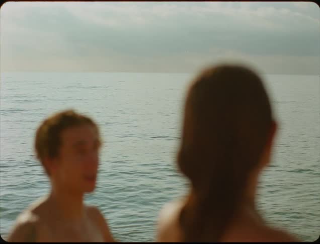 A man raises his hands in expression as he talks to a woman near the water