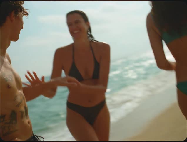 Two women and a man are on a beach playing and flirting