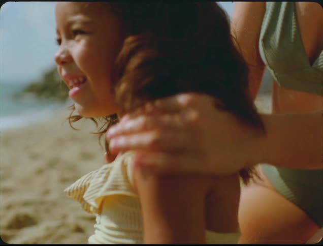A little girl smiles as she waits for her mother to put sunscreen on her at a beach