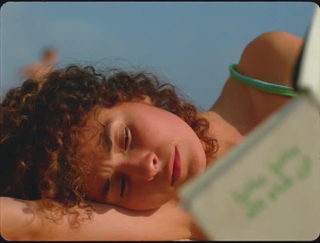 Woman lying on the beach looks at an open notebook under the sun