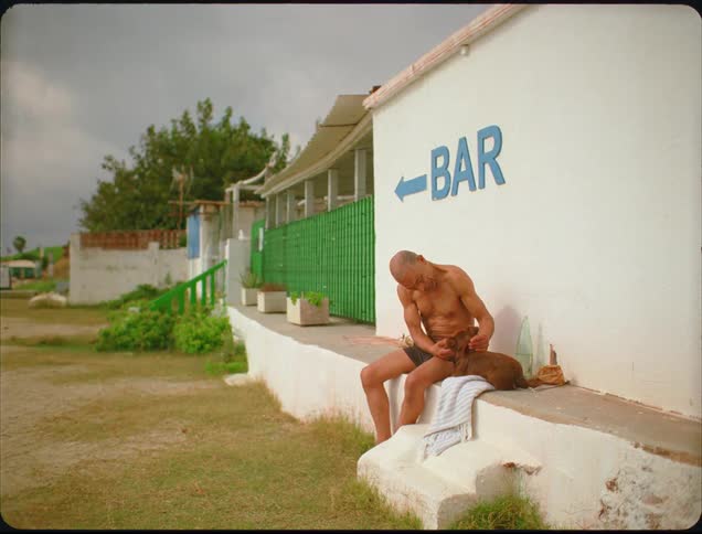 A man sits and petting a dog outside the bar