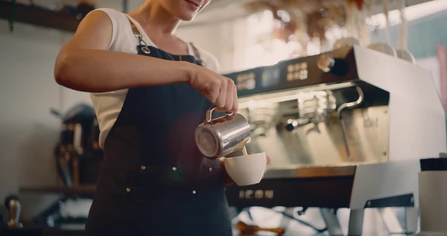 A female barista pours cream into a cup while preparing a caffeinated beverage