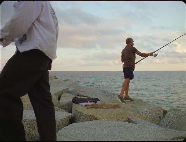 Two men standing on rocks are fishing