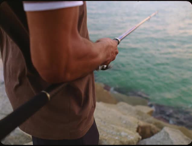 A man is standing on rocks fishing in the ocean