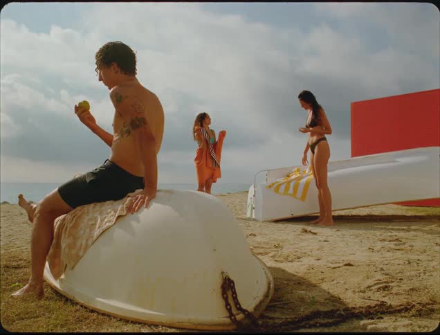 The man eats an apple as two women dry off on the beach