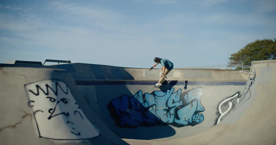 A skateboarder rides a curved ramp in a graffiti covered concrete skatepark on a sunny day