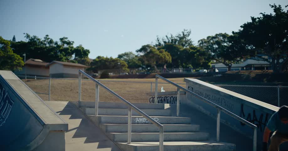 A person skateboards down stairs at an outdoor skate park on a sunny day