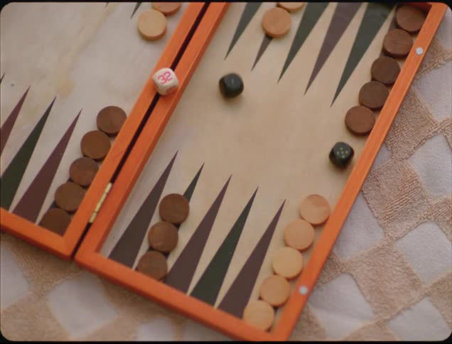 A hand rolls a pair of black dice onto a wooden backgammon board