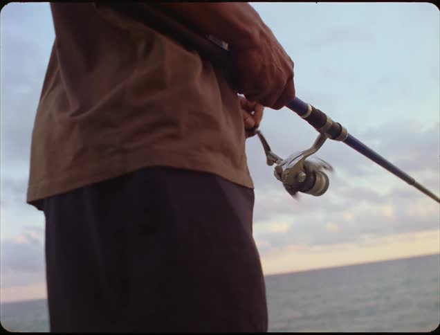 Fisherman cranks the reel of his fishing pole