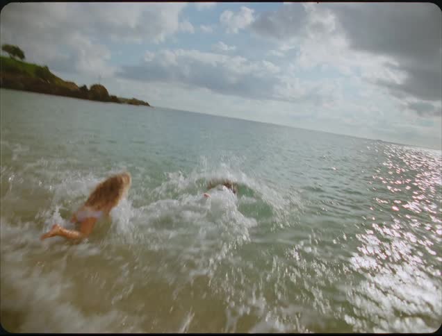Children run across sand toward calm sea under soft late afternoon light