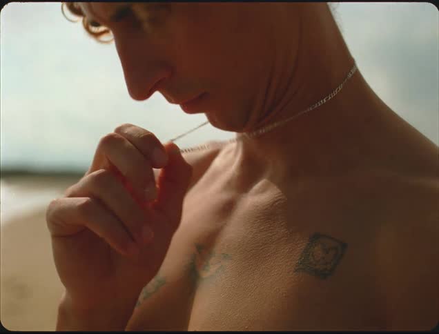 A man standing on the beach at daytime holds his neck chain