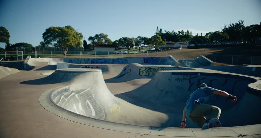 Skateboarder performs frontside grind on bowl edge under blue sky at graffiticovered park