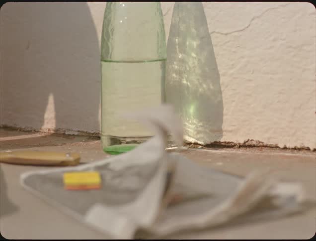 Green bottle on sunlit surface with cast shadow beside blurred newspaper