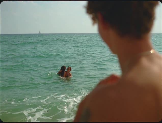 Two women swim in the water while the man watches on the beach