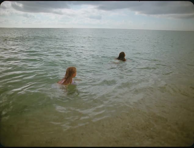 Children play in shallow beach water under partly cloudy sky