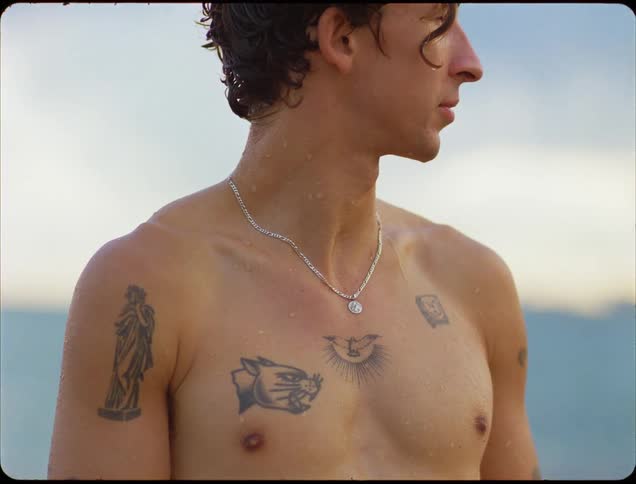 Man with a wet torso shows several tattoos while looking to the side