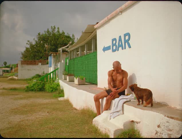 A man sitting outside of a building holds his hands out to beckon a puppy